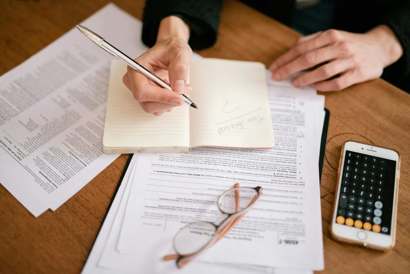 A person writing on top of papers with glasses